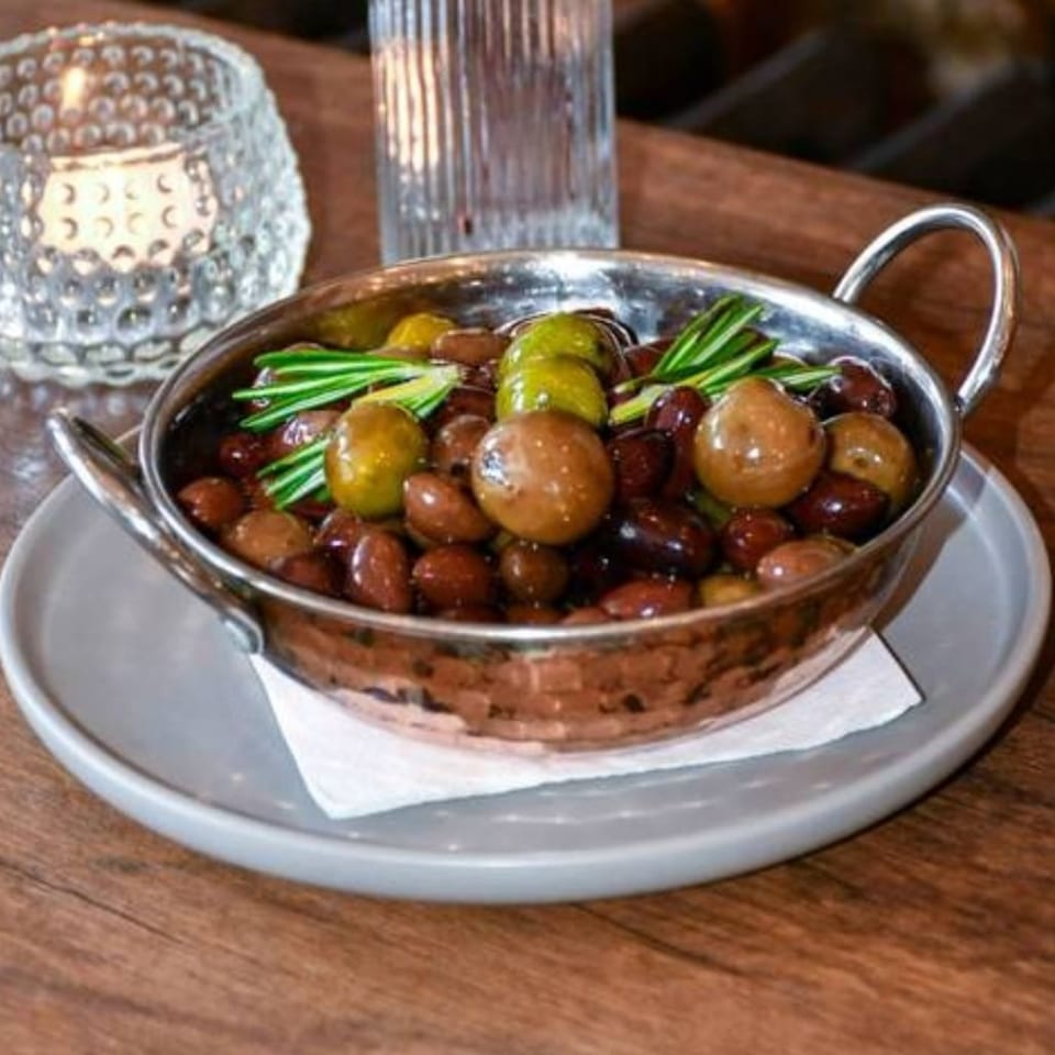 Assorted green and black olives garnished with rosemary in a copper-handled serving dish on a plate.